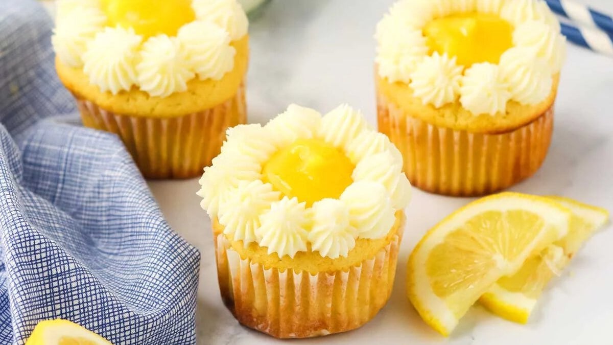 Six cupcakes with yellow centers and white piped frosting are arranged on a black cooling rack.
