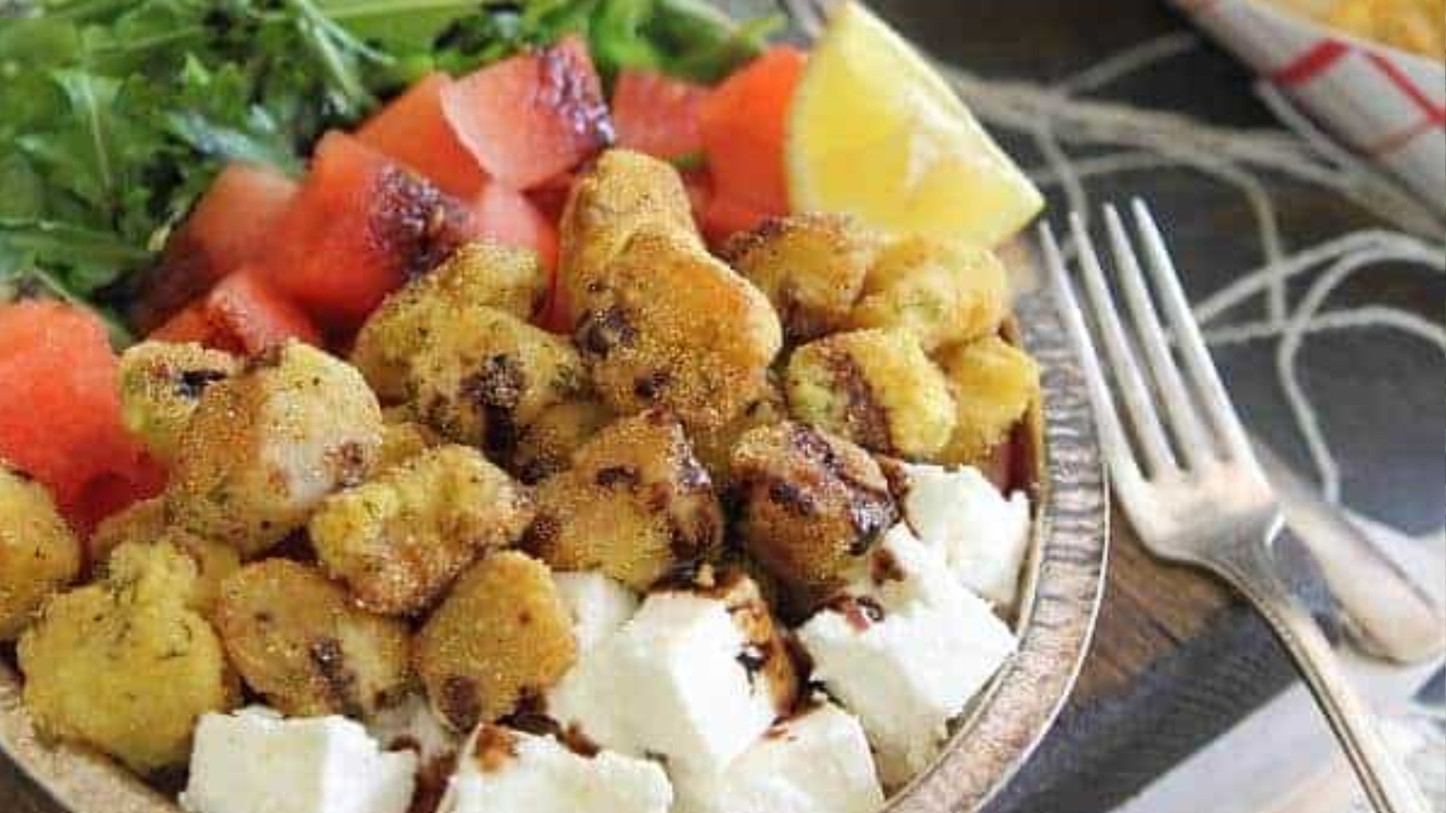 A plate with fried okra, cubed feta cheese, diced watermelon, fresh greens, and a lemon wedge.