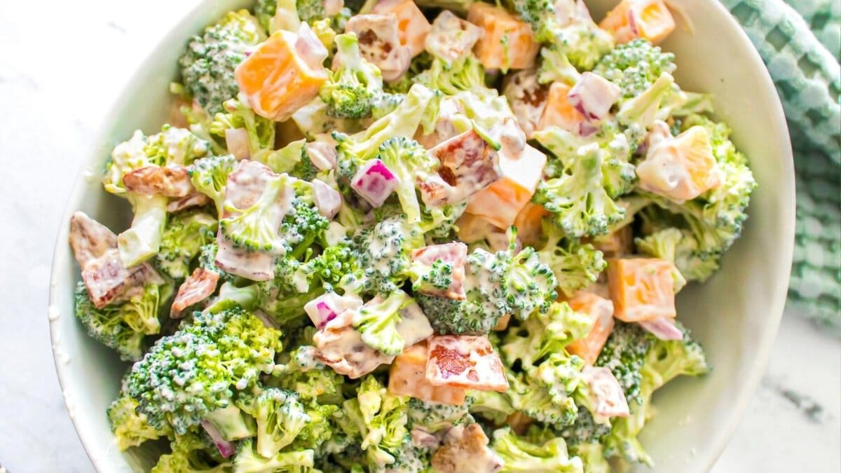 Close-up of a broccoli salad with diced cheddar cheese, red onions, bacon, and creamy dressing.